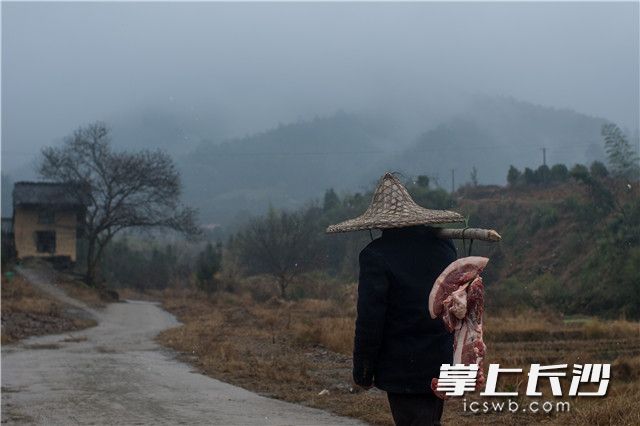 杀年猪后，村民分得五六块猪肉，挑着沉甸甸的乡情回家。