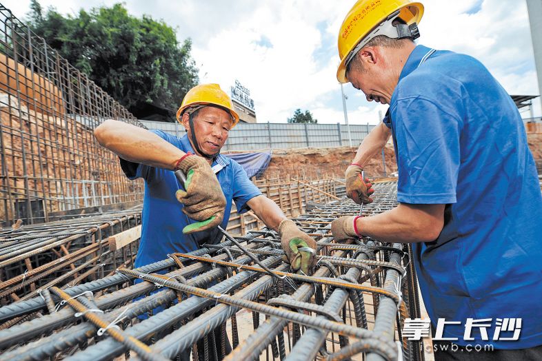 来自重庆的翁昌明(左)和同事在绑钢筋,钢筋被晒得滚烫,他们的工装已被汗水浸湿。 均为长沙晚报记者 王志伟 通讯员 唐炎琰 摄影报道