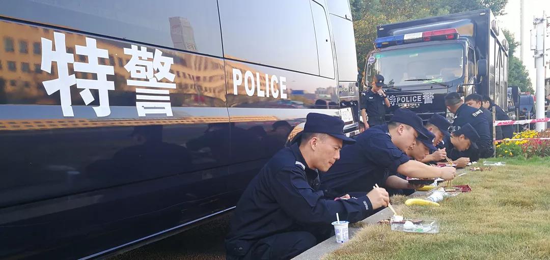 中午时分，一些特警为了不耽误工作，一个个蹲在路边的绿化带旁扒着盒饭。 警方供图