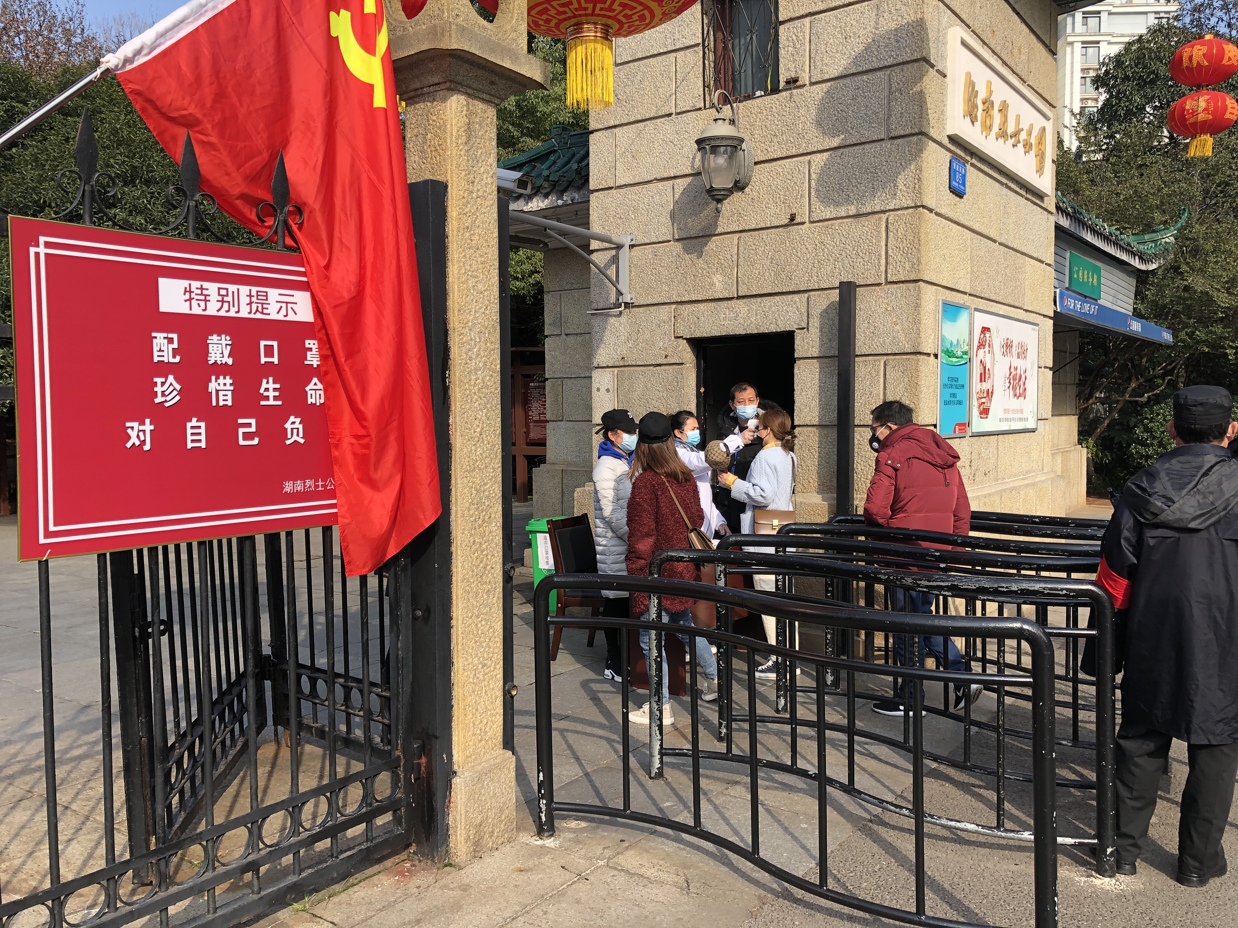 湖南烈士公园工作人员正在劝导入园游客佩戴口罩，并为每位游客测量体温。