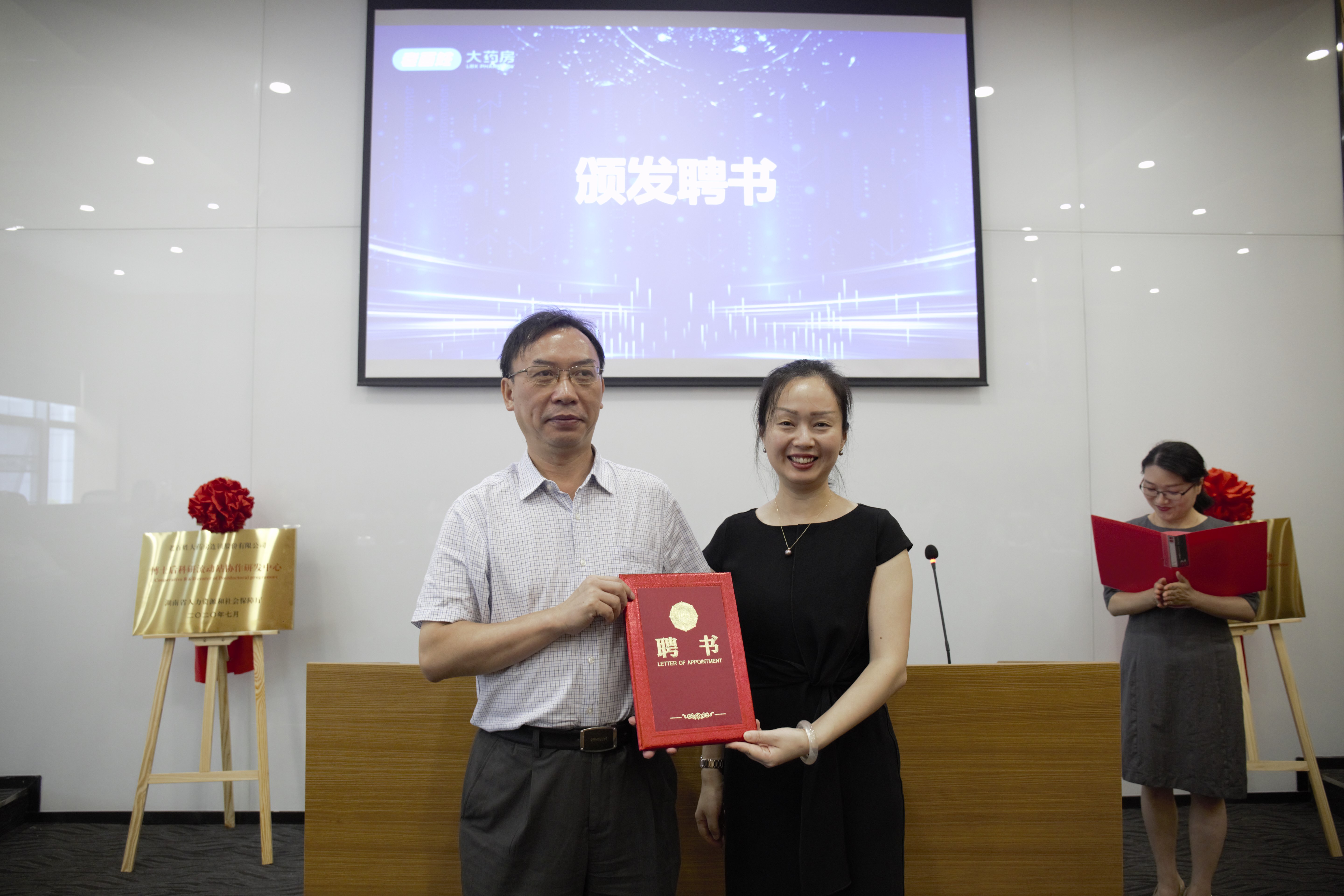 老百姓大药房执行总裁王黎（右）向博士后合作导师——湖南中医药大学副校长、教授何清湖颁发聘书。