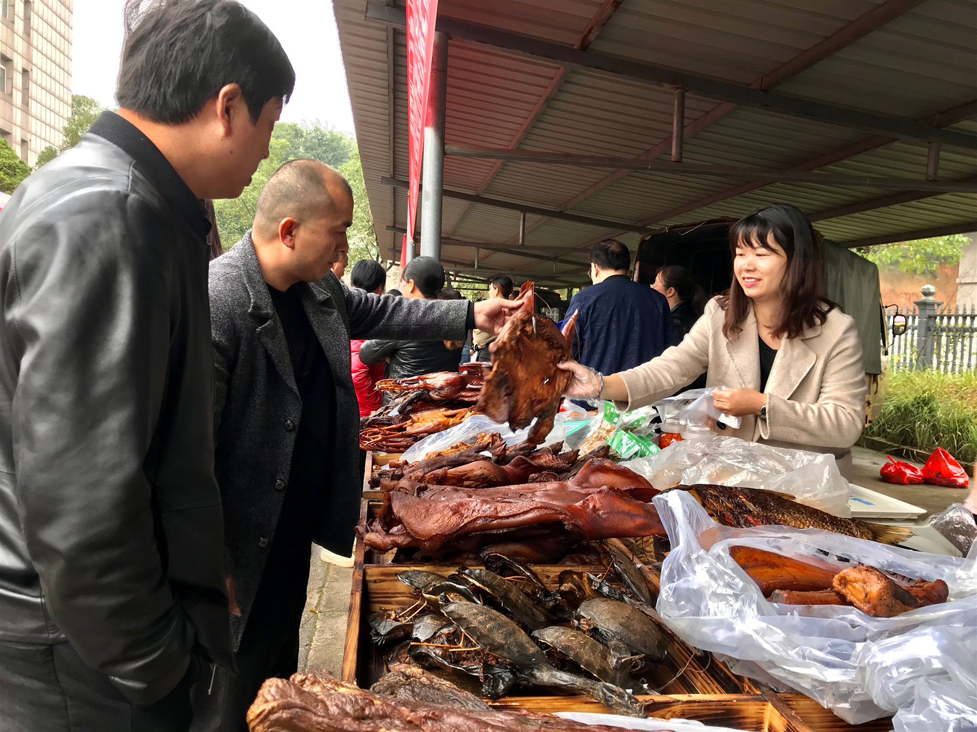 在农产品展销会上，产业项目帮扶单位工作人员正在帮脱贫户们销售自制的腊肉。 长沙晚报全媒体记者 聂映荣 摄