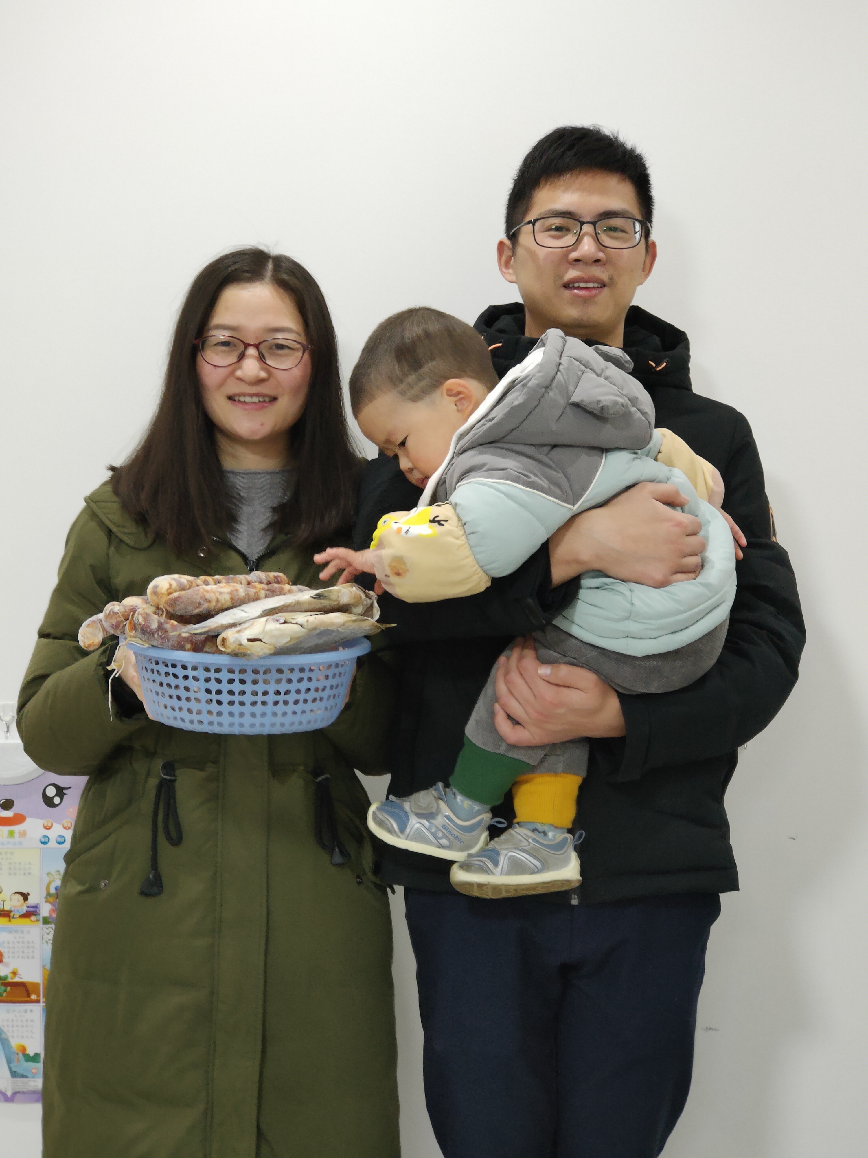 王刘怡一家三口决定留长沙过年，手里端着父亲和公公寄过来的香肠、风干鱼。 受访者供图