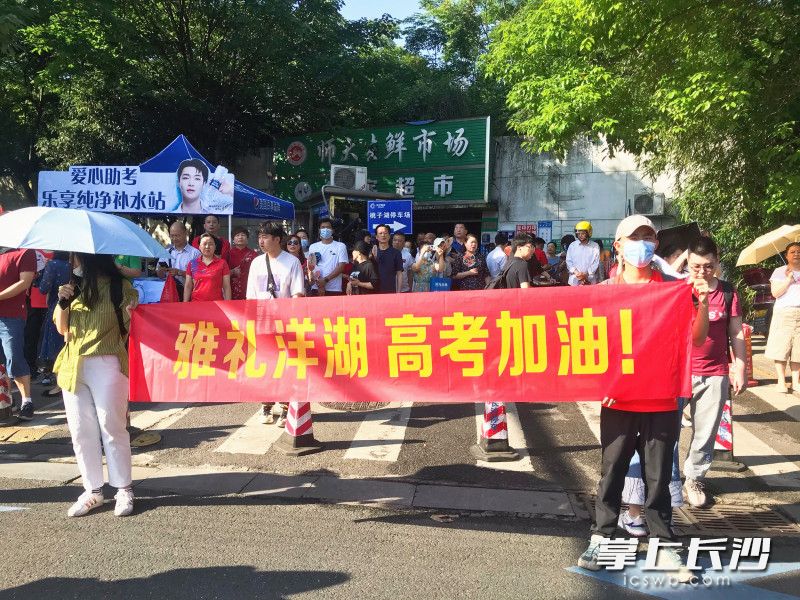 姜奕轩（右）和同学一起手举着“雅礼洋湖 高考加油”的横幅为考生打气加油。全媒体记者 刘俊 摄