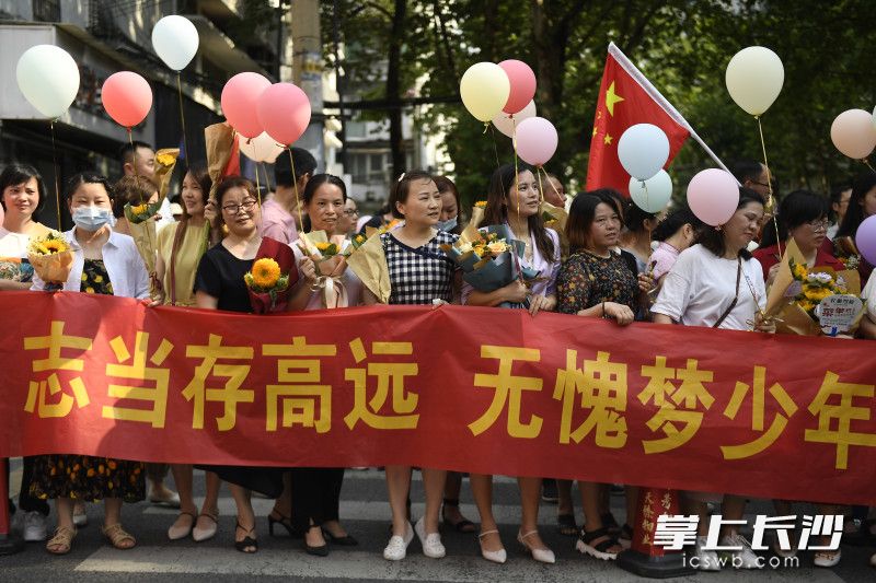在长沙市一中考点，家长们手举鲜花、气球，等待考生们出来。