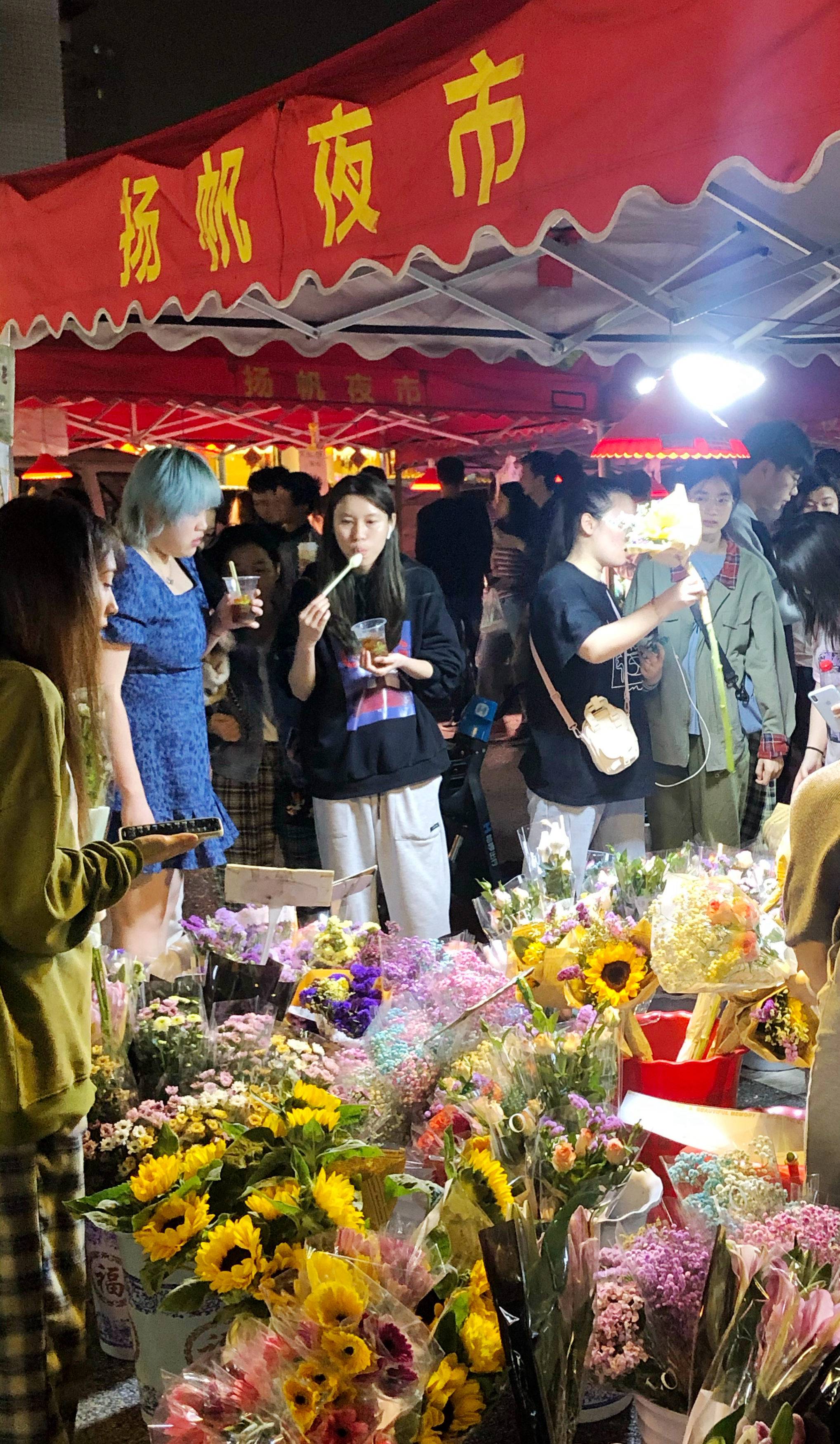 夜市里，琳琅满目的商品应有尽有，游客正在选购物美价廉的鲜花。