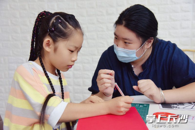 一名女生在老师指导下剪纸。