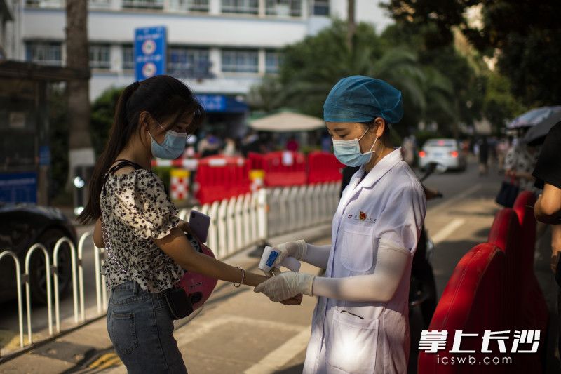 在医院核酸检测入口，医护人员在给进入人员进行体温测量。