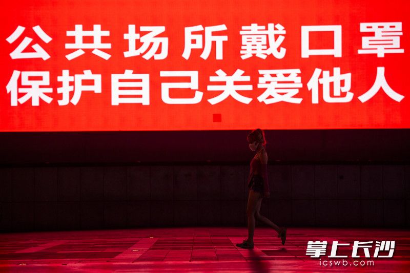 市民在黄兴广场走过，一旁的大屏上，提醒着戴着口罩关爱他人更保护自己。