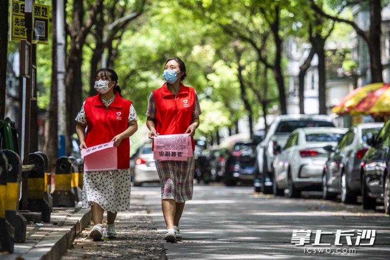 志愿者罗娟（左）和张倩倩（右）在社区内进行防治疫情宣传提示的粘贴。罗娟是98年出生，倩倩是99年出生，疫情发生以来，她俩第一时间参与志愿服务，协助街道开展人员劝导等工作，一天时间走了2万多步，要喝7-8瓶水。 