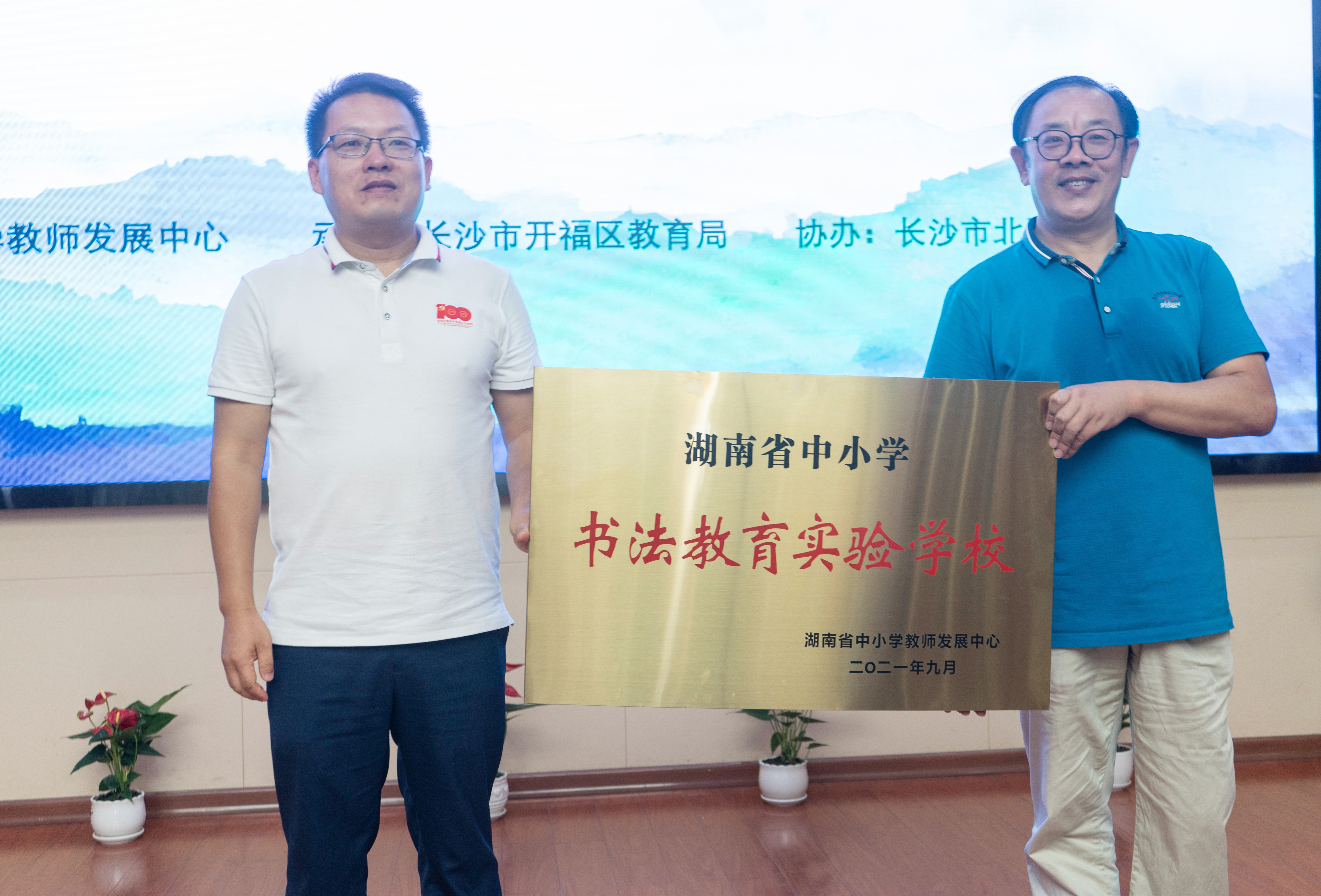 北雅中学校长吴志勇（右）从湖南省中小学教师发展中心副主任曾建军手中接过“湖南省中小学书法教育实验学校”牌匾。    长沙晚报通讯员 肖克 摄