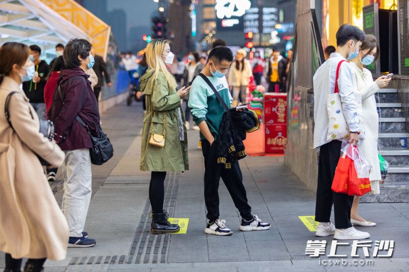 在长沙黄兴南路步行商业街上，几位路人戴着口罩正在排队买小吃。全媒体记者 董阳 摄