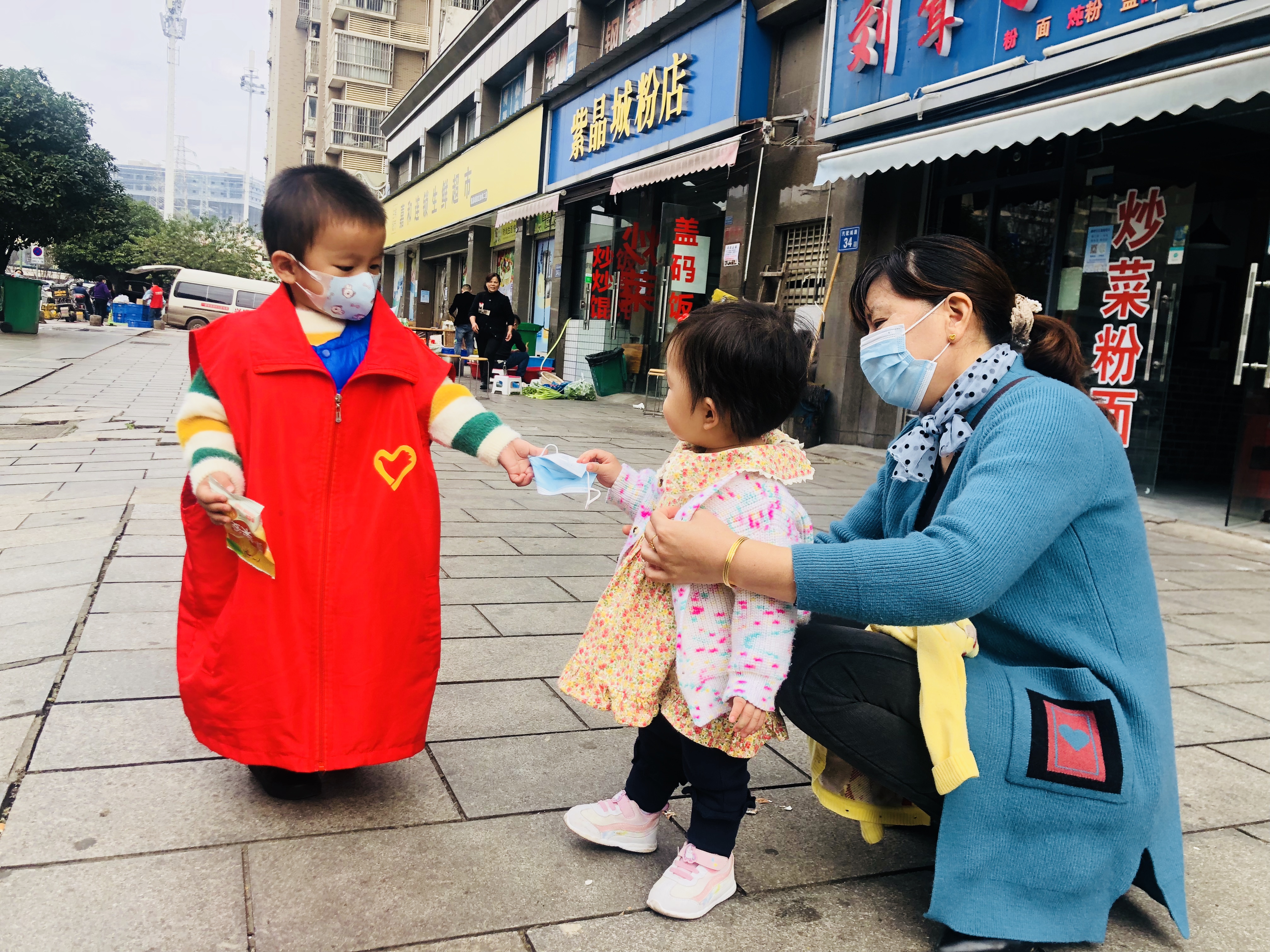 26日，跟着妈妈来“上班”，3岁萌娃志愿者邹涵睿给没佩戴口罩的居民送口罩。