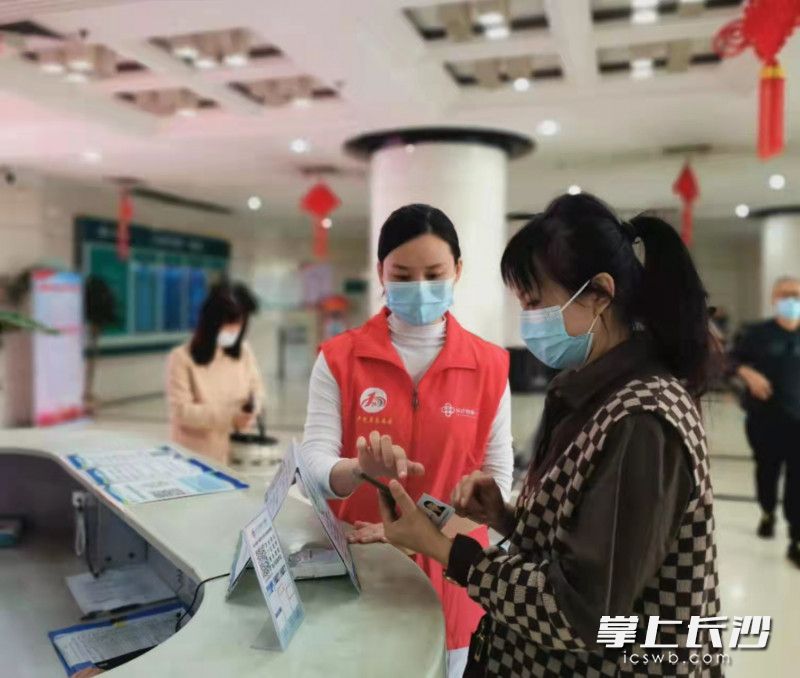长沙市第一医院门诊大厅的志愿者帮助群众在手机上如何进行便捷就医的操作。医院供图
