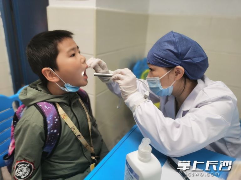 在开福区福元小学接种点预检室，医务人员给史家坡小学四（6）班学生侯世力小朋友检查喉咙。