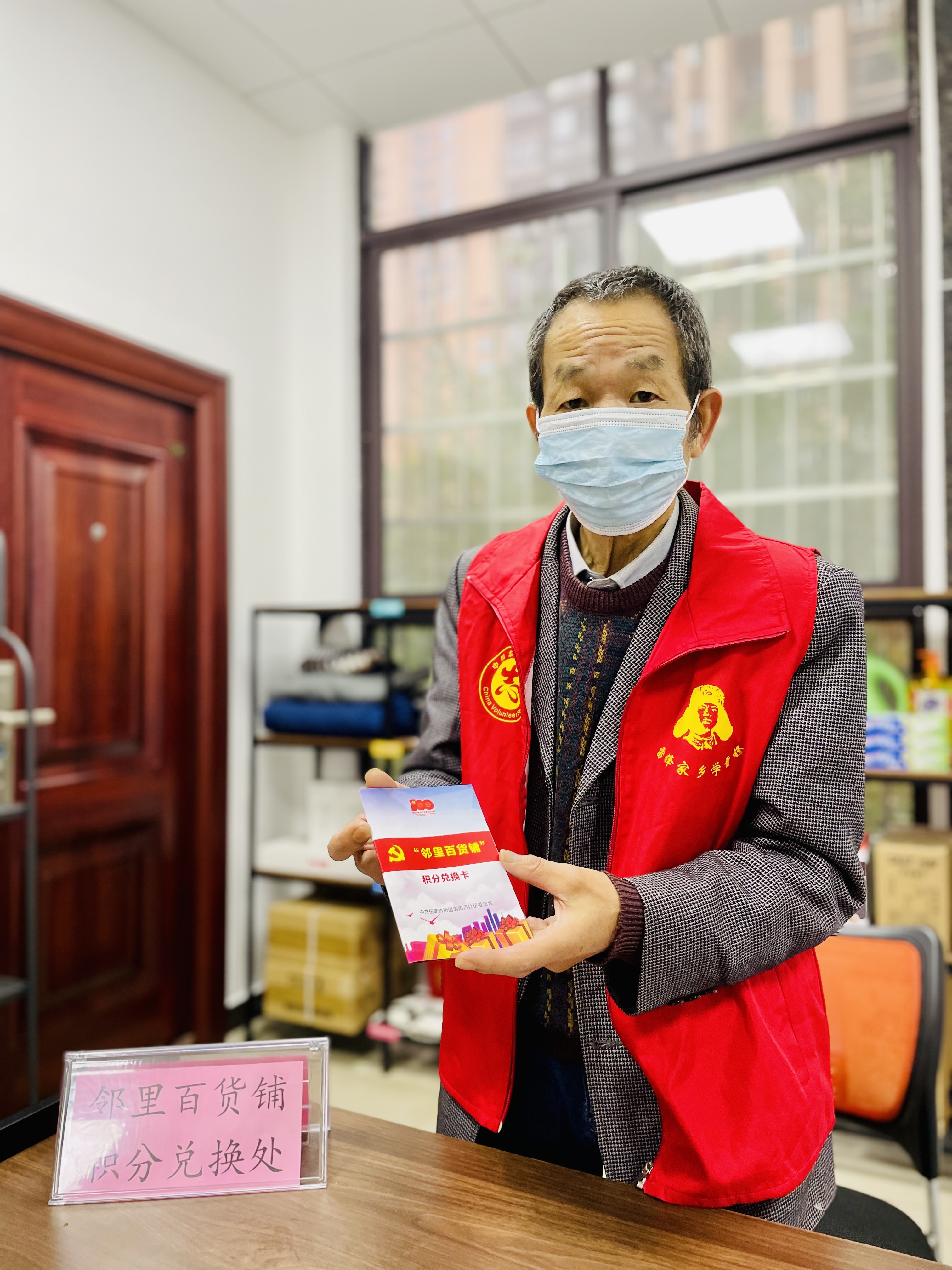 轮值“掌柜”展示积分卡，做志愿服务攒积分，公租房住户就能兑换他身后这些百货物资。 全媒体记者 李卓 摄