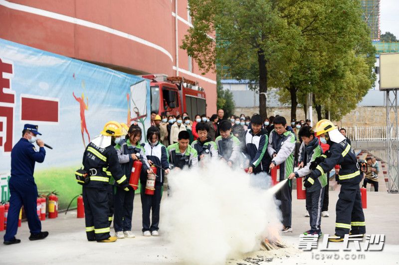 鹅秀中心消防救援站消防员教中学生使用干粉灭火器灭火。