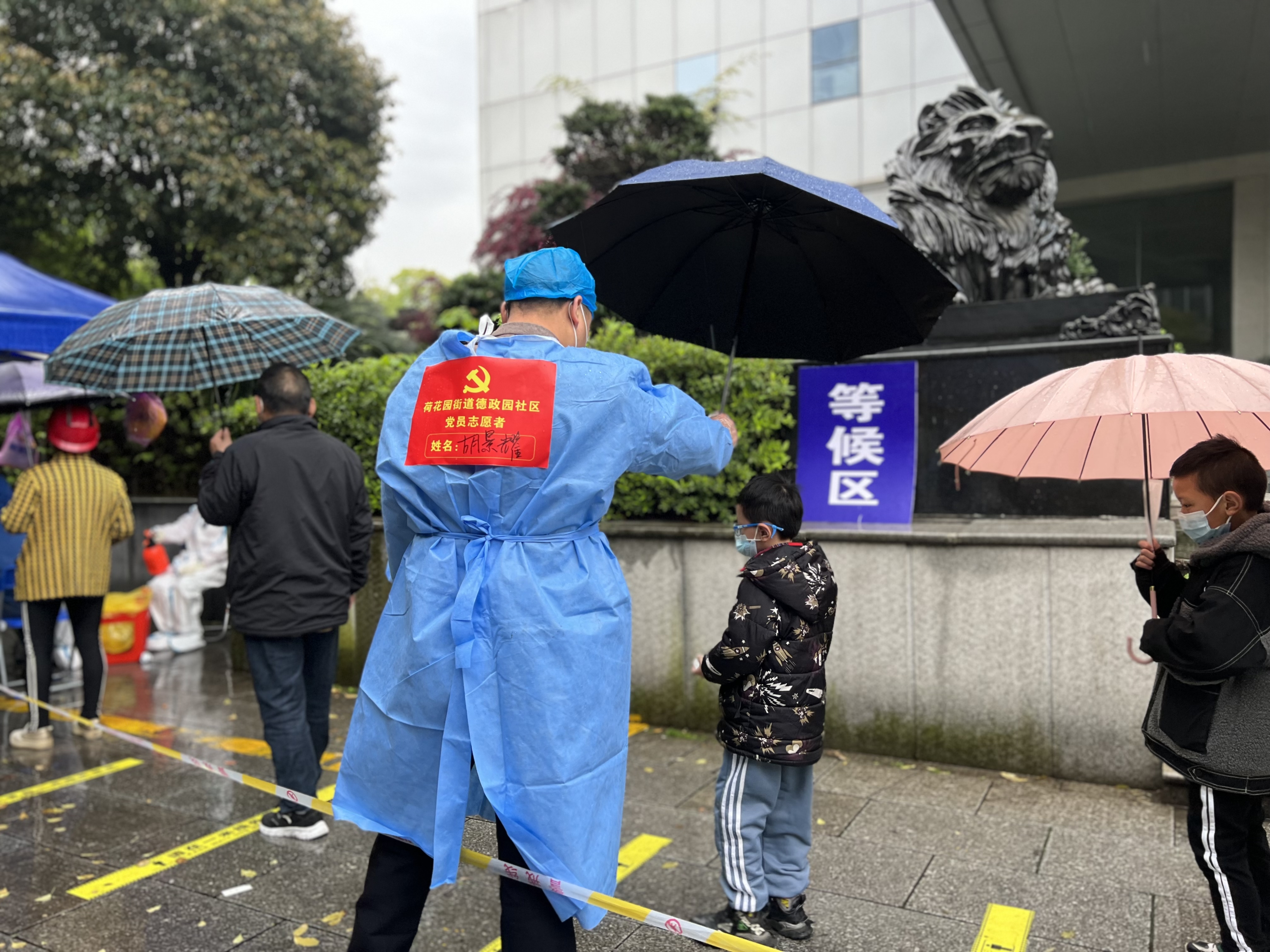 党员志愿者胡景耀将自己的雨伞朝小男孩头上移了过去，并与他保持着1米安全距离。长沙晚报通讯员 周淑摄