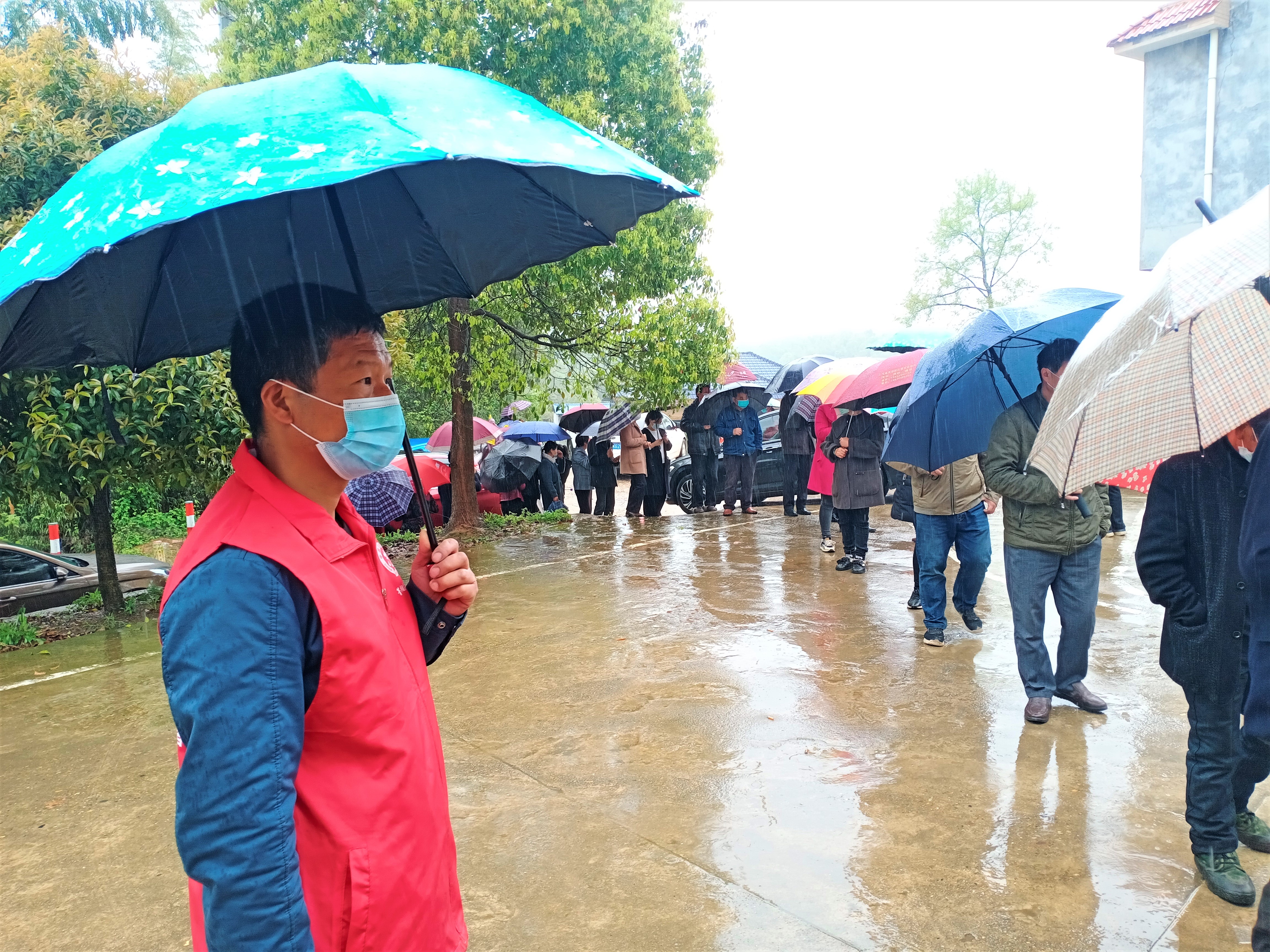 在宁乡市菁华铺乡嶂山村的核酸检测点，身穿红马甲的党员志愿者杨建知一边撑着雨伞，一边用略显嘶哑的声音喊着维持秩序。长沙晚报全媒体记者 张禹 通讯员 易杰 摄影报道