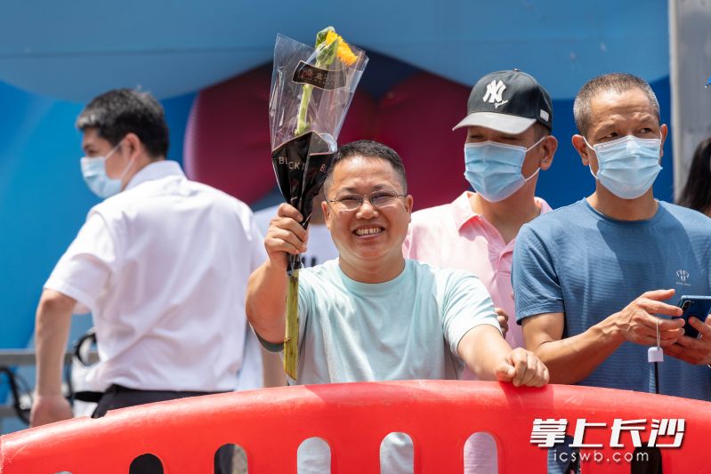 一位家长手持向日葵露出微笑，祝福自己孩子2022年高考“一举高中”。