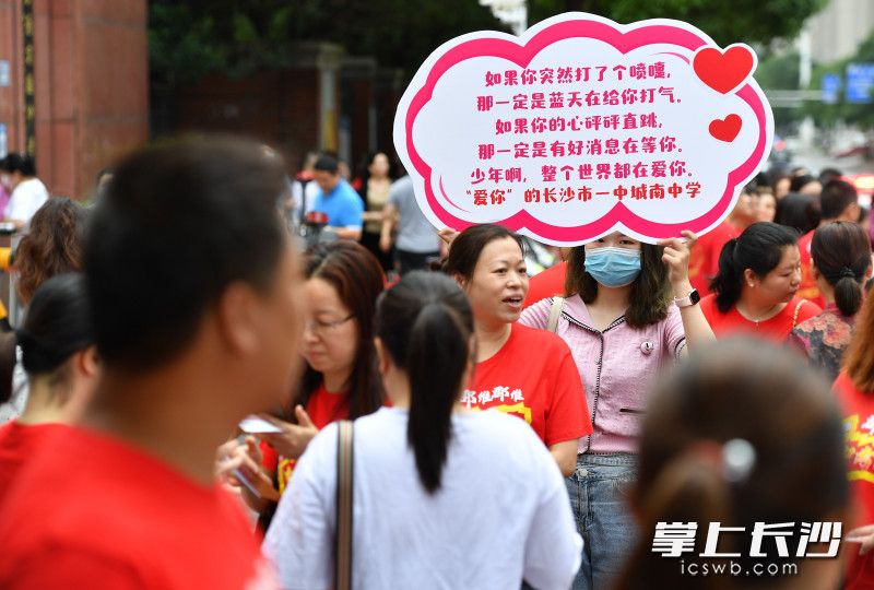 长沙市长郡双语实验中学外，一位女士举着“应援牌”为考生加油。长沙晚报全媒体记者 郭雨滴 摄