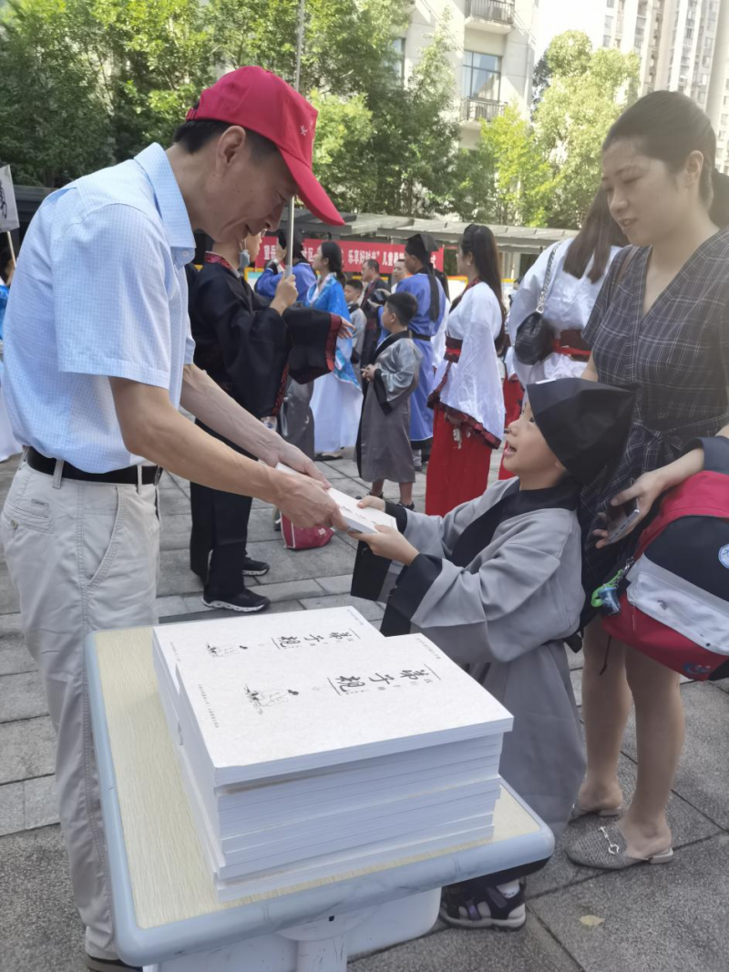 图为开营仪式上，党员志愿者（左）为孩子分发国学经典书籍。  长沙晚报通讯员 供图