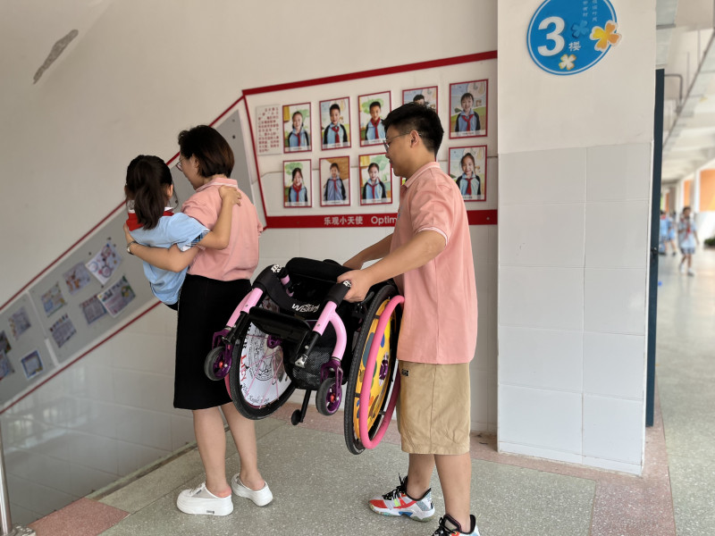 每天放学后，一位老师拿轮椅，一位老师抱小艺下楼。均为长沙晚报通讯员 周起家 供图