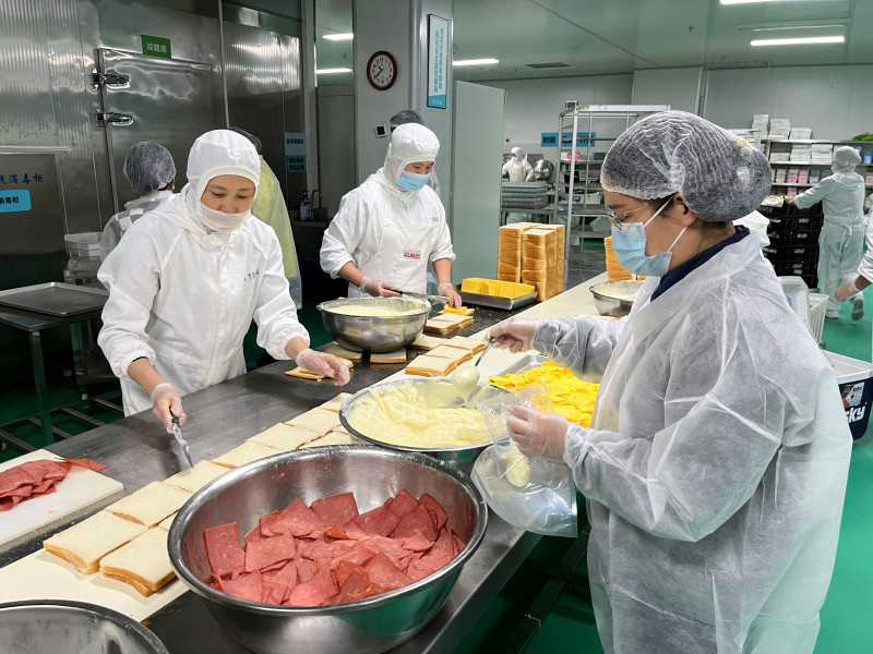 疾控人员（右一）在蛋糕店制作车间进行食品安全风险监测采样。