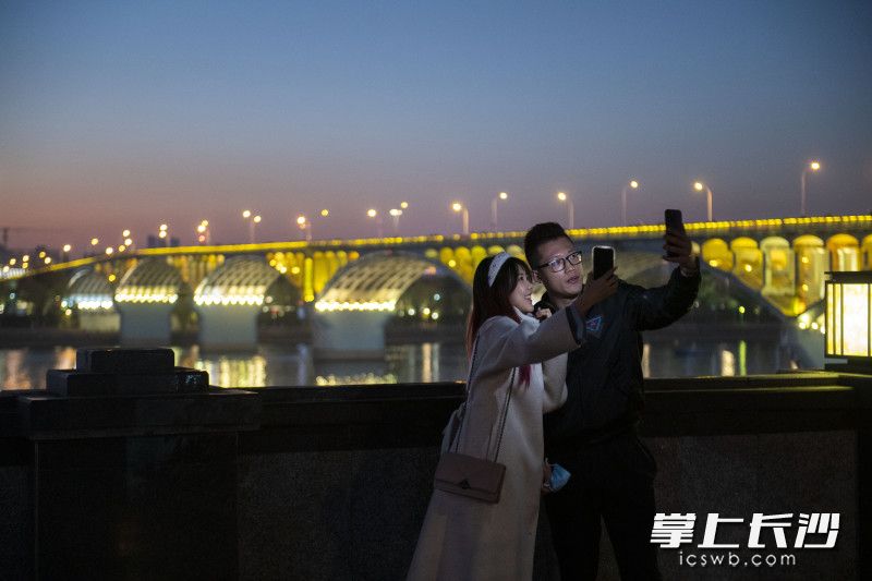 游客与夜幕下的橘子洲大桥合影。