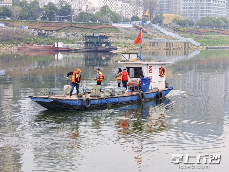 志愿者登上小船清理漂浮在河面上的垃圾。