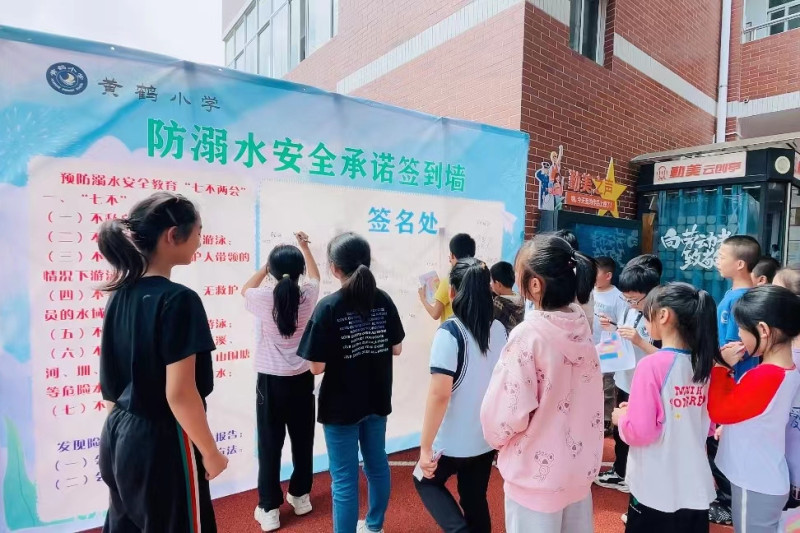 同学们纷纷在防溺水安全承诺签到墙上签名。