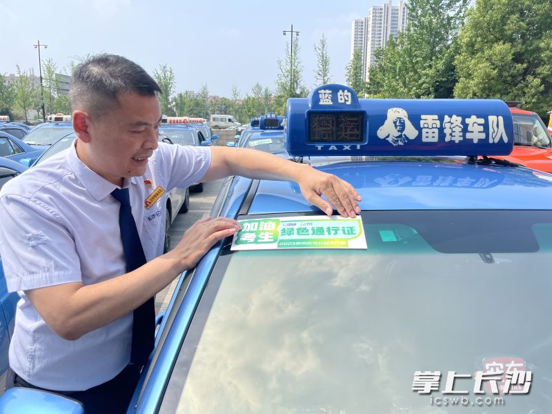 出租车驾驶员彭友良在领取“爱心送考绿色通行证”，将其贴在出租车上。