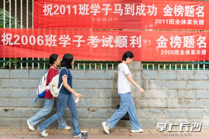 开考前，三位考生从考场外的加油横幅旁经过。