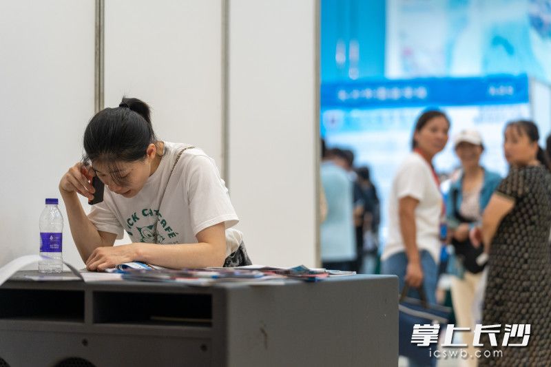 活动角落，一位母亲正在与家人电话沟通分享在中考咨询会上得到的信息。