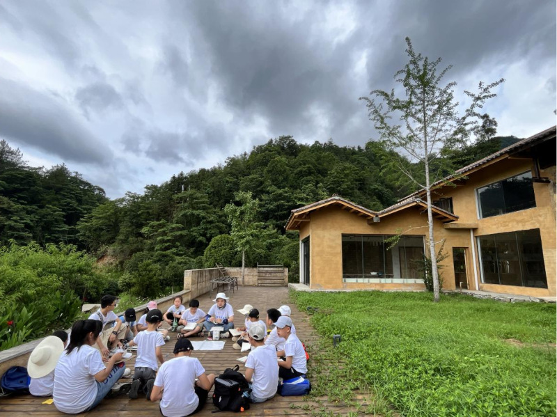 在道官冲古法造纸研学馆前坪，孩子们席地而坐，讨论自己采访所得的与造纸相关的信息，并与西米老师一起整理造纸工艺流程图。
