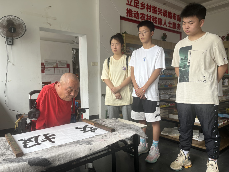 “半截人”周国民用嘴叼笔，给两位“准大学生”（右一、右三）写下“报效祖国”的青春寄语。  均为长沙晚报全媒体记者 黎铁桥 摄