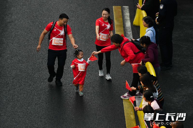 在浏城桥下，一位小选手跑过时，一位加油的观众为她递过来一面国旗。