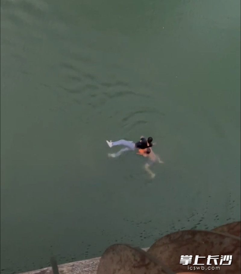 成维在水中展开救援，将救生浮球放在男子头部下方。视频截图