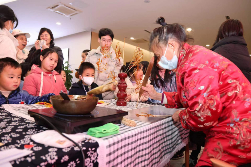 在糖画桌前，老师以勺子为“笔”、糖稀为“墨”，在光滑的石板上飞快地描摹。