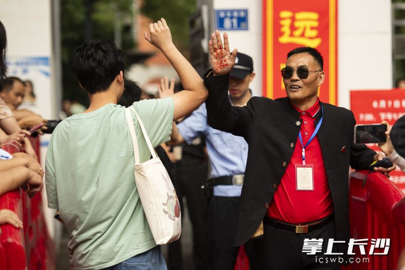 长沙市一中校保卫科孙科长在手掌上写着“加油”，与考生击掌。