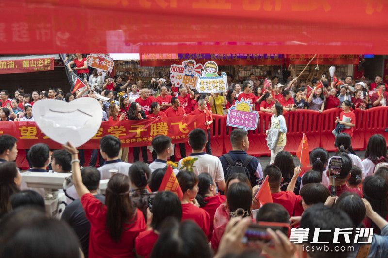 送考老师和家长身着红色服装，举着红旗或应援牌，为考生助威。  均为长沙晚报全媒体记者郭雨滴摄