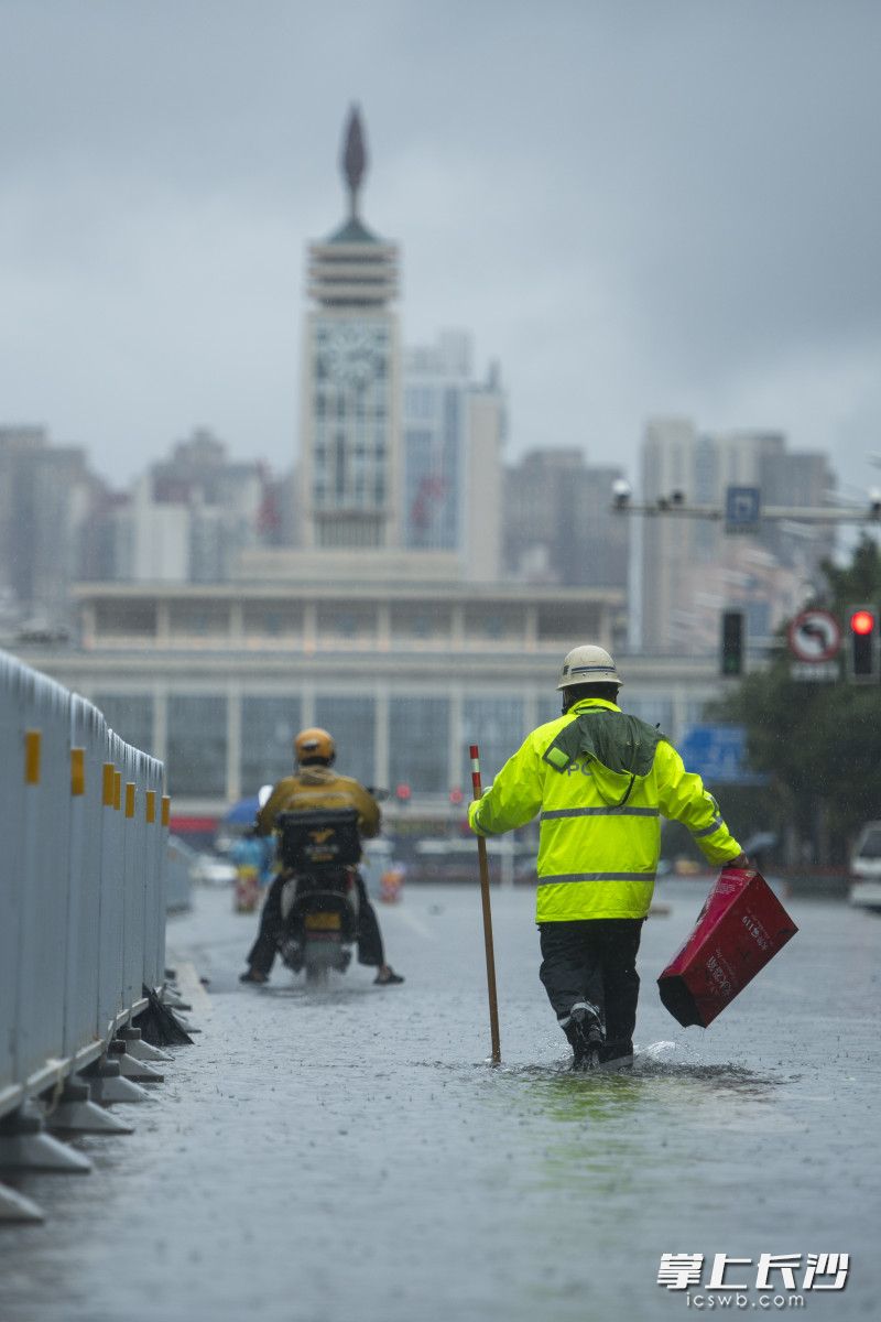 6月24日14时11分，五一大道一处积水路段水位快速下降，一位芙蓉交警拿着木棍试探水深，以考虑车辆可否通行，还不时捡起路面杂物。