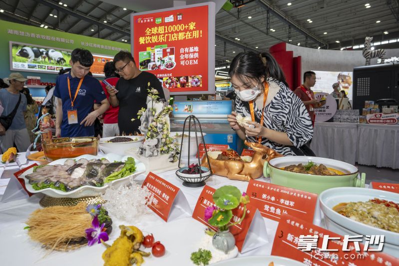 湖南展区里，一观展市民手拿肉包认真观看着湘菜大厨们的参赛作品。