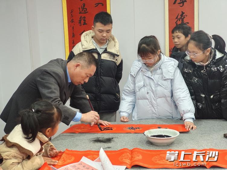 一位书法艺术家正在写春联，吸引了多位小朋友围观。均为长沙晚报通讯员李丽芳 宗泽慧 供图