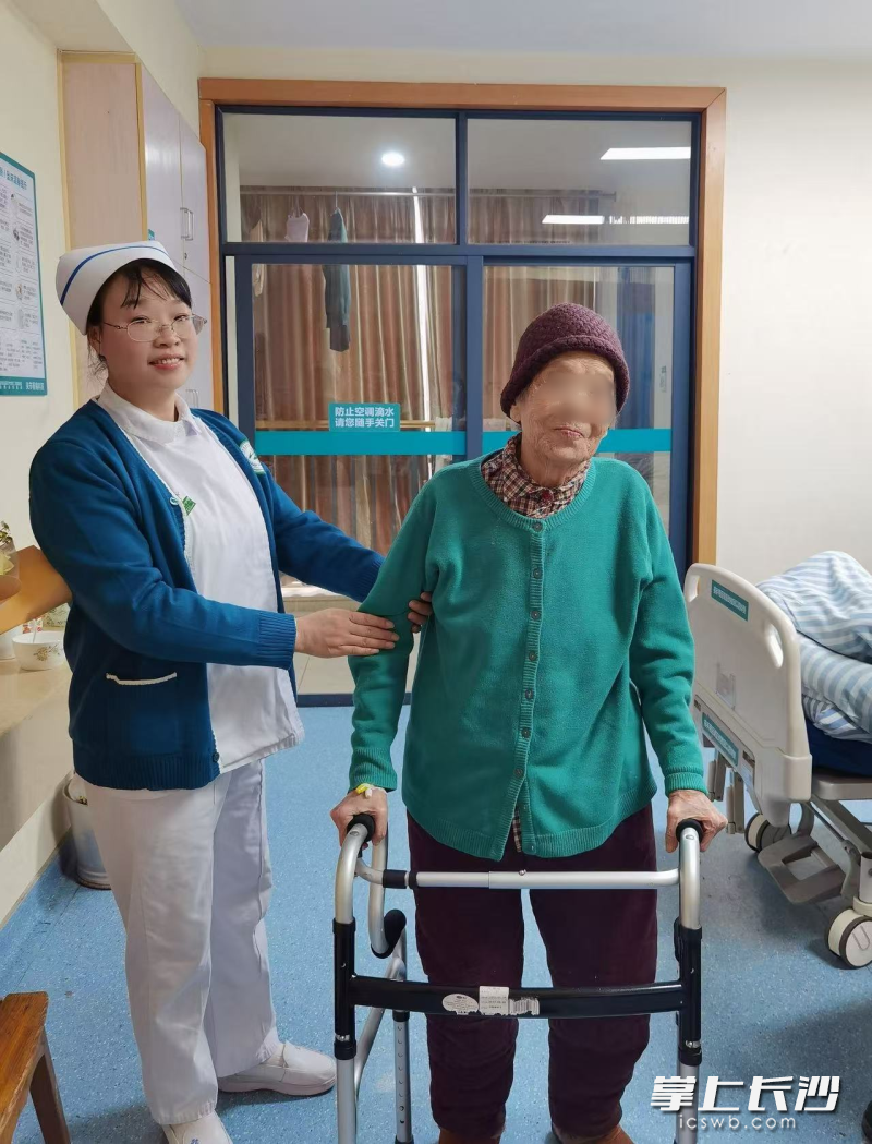 护理人员在协助百岁老人进行术后的康复训练。
