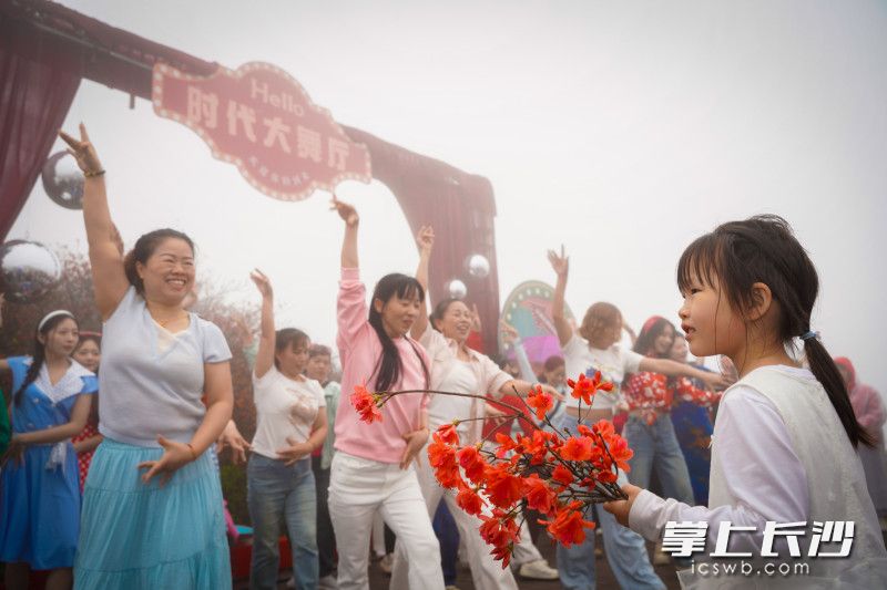 现场一位小女孩手捧着杜鹃花，津津有味地欣赏着“时代大舞厅”里大家的即兴舞蹈。