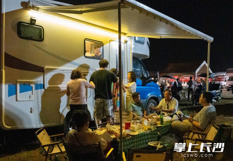 游客们惬意的坐在房车下，吹着晚风，品尝美食。