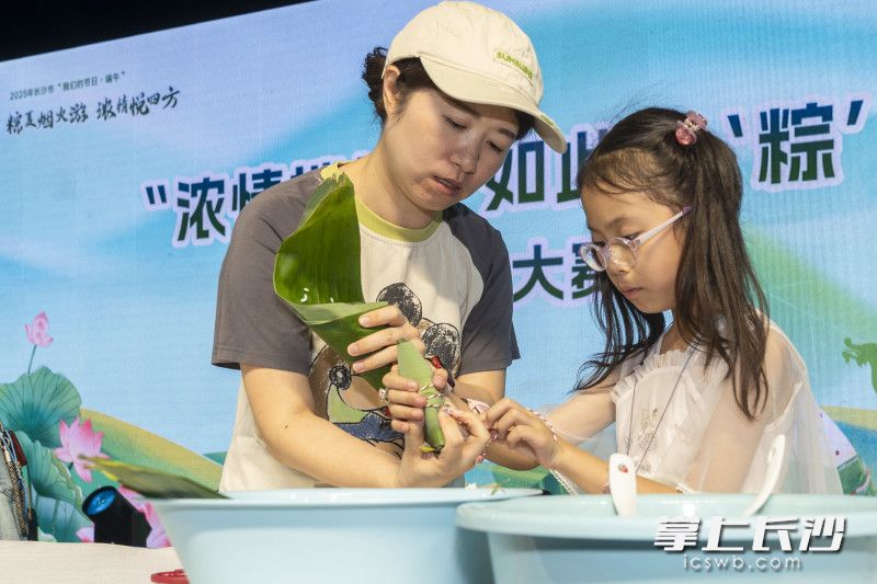 29日晚，四方商贸城夜市，参加包粽子比赛的小选手，认真地学着大人的模样包粽子。 长沙晚报全媒体记者 周数邑 摄