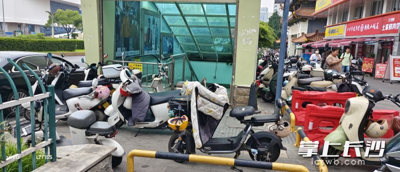 在长沙东塘大都市商业街的多个出入口，密密麻麻挤满了电动车和共享单车，将出入口堵得严严实实。