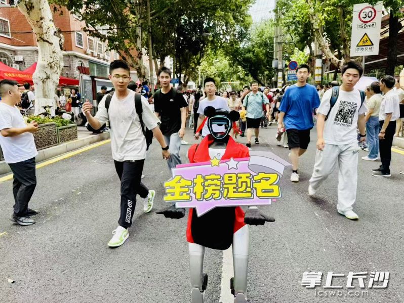 “笨笨”高举“金榜题名”海报，送考生们进考点。